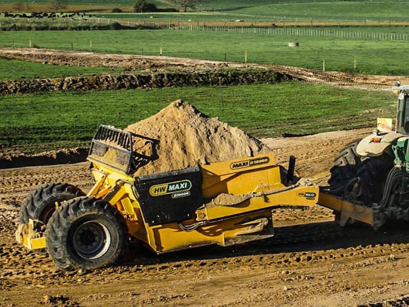 Yellow construction scraper being pulled by a tractor on a field.