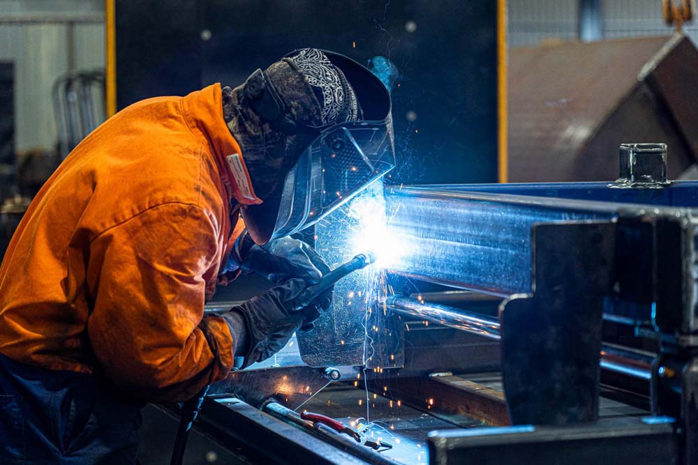 Welder in orange safety gear welding metal parts.